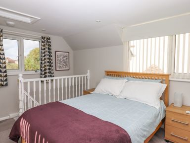 A bedroom with a double bed bedside table and windows with curtains at Wisteria Cottage in Exmouth