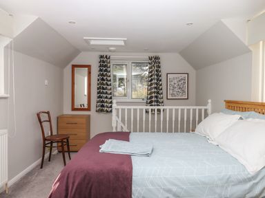 A bedroom with a bed pillow and blanket a wooden chair a dresser a mirror and patterned curtains at Wisteria Cottage in Exmouth