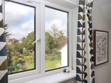 A window with patterned curtains looking out to a garden and houses at Wisteria Cottage in Exmouth