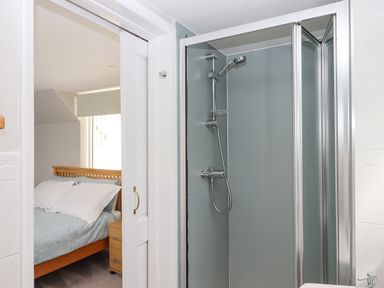 A bathroom with a shower enclosure and a view into a bedroom with a wooden bed and bedside drawer at Wisteria Cottage in Exmouth