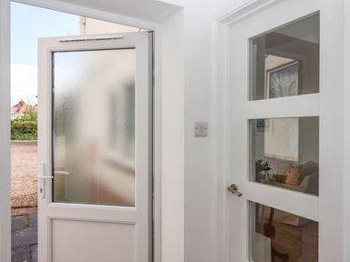 An open white frosted glass door leading outside and a white interior door with glass panels at Wisteria Cottage in Exmouth