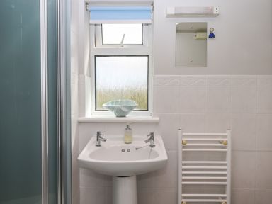 A bathroom with a sink soap dispenser small mirror window and towel radiator at Wisteria Cottage in Exmouth