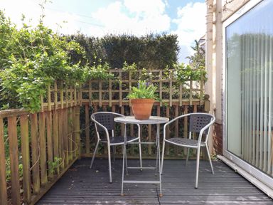 An outdoor patio with two metal chairs a round table and a potted plant on the table at Wisteria Cottage in Exmouth