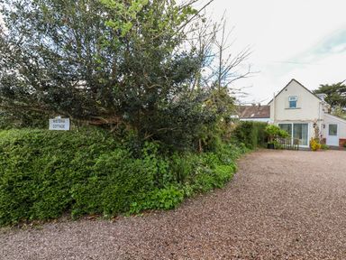 A driveway with gravel leading to a white house with a sliding door and plants along the sides at Wisteria Cottage in Exmouth