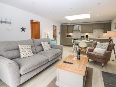 An open living room and kitchen with a gray sofa, brown armchair, wooden coffee table, and dining table with chairs at Rabbits Warren in Titchfield Common