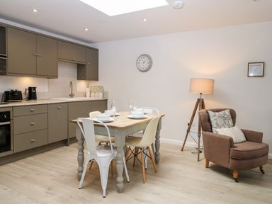 A kitchen with a dining table set with bowls and glasses next to an armchair and floor lamp at Rabbits Warren in Titchfield Common