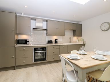 A kitchen with brown cabinets a wooden table set with bowls and glasses and a clock on the wall at Rabbits Warren in Titchfield Common