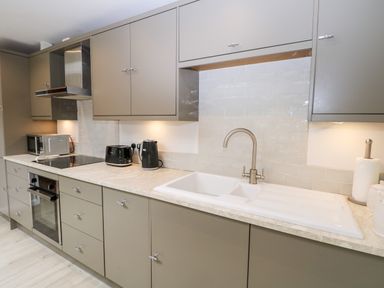 A kitchen with gray cabinets a white sink black toaster and kettle a microwave and an oven at Rabbits Warren in Titchfield Common