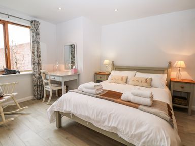 A bedroom with a bed and bedside tables with lamps a desk with a chair a mirror and a rocking chair at Rabbits Warren in Titchfield Common