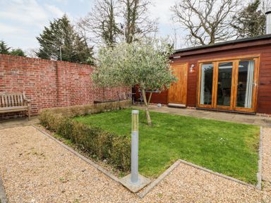 A backyard with a small tree on a grassy area surrounded by gravel paths and a wooden bench near a brick wall at Rabbits Warren in Titchfield Common