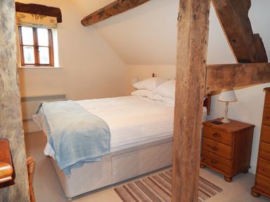 A bedroom with a double bed wooden furniture and visible wooden beams at The Granary Walford near Ross-on-Wye