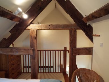 An attic space with wooden beams a wooden chest of drawers a wicker chair and a wooden railing at The Granary in Walford near Ross-on-Wye