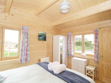 A bedroom with wooden walls ceiling bed with towels and blue blanket wardrobe dresser and windows at The Shippen in Merriott