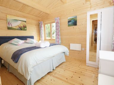 A bedroom with a bed two pillows two rolled towels a window a white wardrobe and wooden walls at The Shippen in Merriott