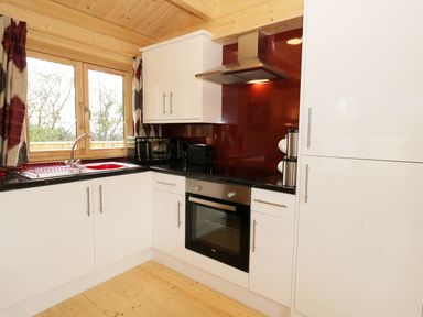 A kitchen with white cabinets a black countertop a red backsplash and wooden window frames at The Shippen in Merriott