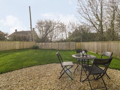 A backyard with a gravel patio, a round table and four chairs with a bottle and glasses on the table at The Shippen in Merriott