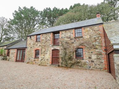 A stone cottage with multiple windows and wooden doors surrounded by trees at Barn Cottage in Marazion