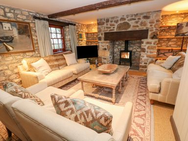 A living room with stone walls two sofas an armchair a wooden coffee table and a fireplace with a wood stove at Barn Cottage in Marazion