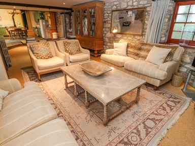 A sitting area with armchairs sofas a wooden coffee table and a cabinet in a room with stone walls and a window at Barn Cottage in Marazion