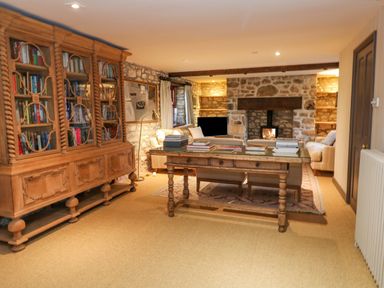 A living room with a large wooden bookshelf a table with books and a stone fireplace at Barn Cottage in Marazion