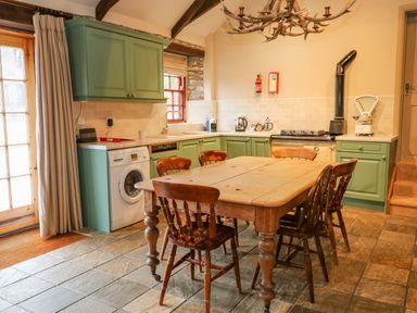 A kitchen with green cabinets a wooden table with six chairs and stone floor at Barn Cottage Marazion