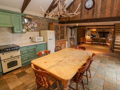 A kitchen and dining area with a wooden table and chairs a stove refrigerator and green cabinets at Barn Cottage in Marazion