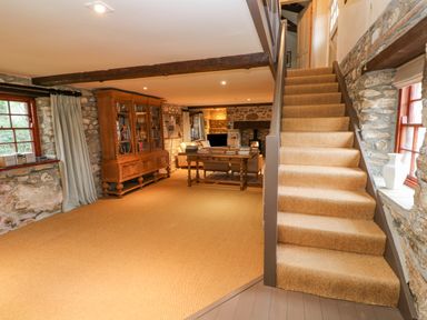 A living area with stone walls a carpeted staircase wooden bookcase and a wooden table with books at Barn Cottage Marazion