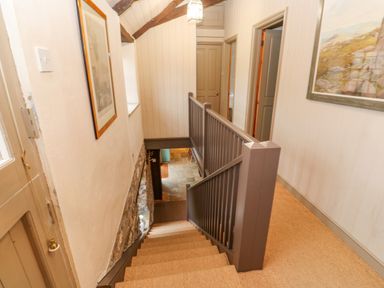 A staircase with a brown railing and carpeted steps in a hallway with doors and framed pictures on the walls at Barn Cottage in Marazion