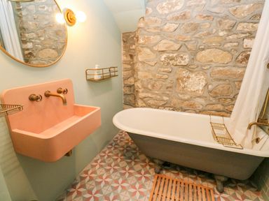 A bathroom with a stone wall clawfoot bathtub pink sink and patterned tile floor at Barn Cottage in Marazion