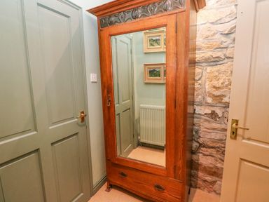 A wooden wardrobe with a mirrored door between two doors and a stone wall at Barn Cottage in Marazion