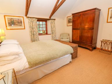 A bedroom with a bed a large wooden wardrobe a cushioned chair and framed artwork at Barn Cottage in Marazion