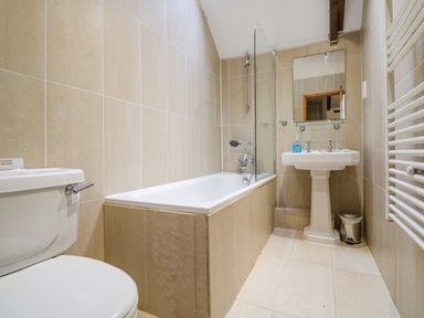 A bathroom with a toilet bathtub sink mirror and towel radiator at Barn Cottage Marazion