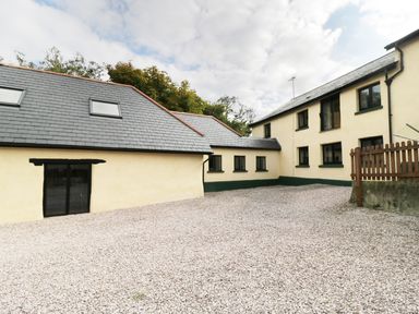 A courtyard with gravel ground and yellow buildings with black windows at Carthorse Cottage in Teignmouth