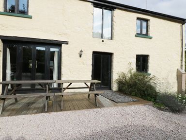 Exterior view of a building with cream walls black framed windows and doors wooden picnic table on a wooden deck at Carthorse Cottage in Teignmouth