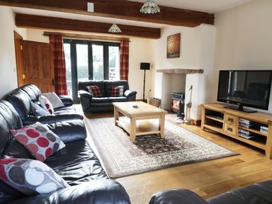 A living room with black leather sofas a wooden coffee table a TV on a wooden stand and a fireplace at Carthorse Cottage in Teignmouth