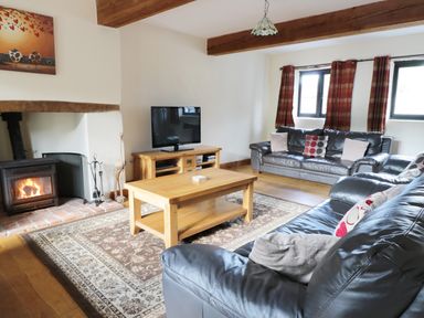 A living room with leather sofas a wooden coffee table a fireplace a television and wooden beams on the ceiling at Carthorse Cottage in Teignmouth