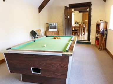 A room with a pool table a small tv on a cabinet a wooden bookshelf and chairs at Carthorse Cottage in Teignmouth