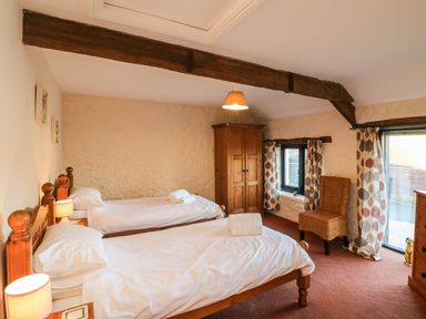 A bedroom with two single beds wooden furniture a chair and patterned curtains at Carthorse Cottage in Teignmouth