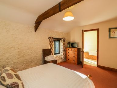 A bedroom with a bed a chest of drawers a chair with towels and a view into a bathroom at Carthorse Cottage in Teignmouth
