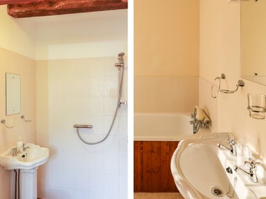 A bathroom with a white sink, shower head, bathtub with wooden panel and mirror at Carthorse Cottage in Teignmouth