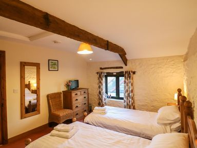 A bedroom with two single beds a wooden chest of drawers a wicker chair and a small window at Carthorse Cottage in Teignmouth