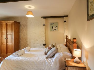 A bedroom with a wooden bed and wardrobe two rolled towels on the bed and a lamp on a bedside table at Carthorse Cottage in Teignmouth