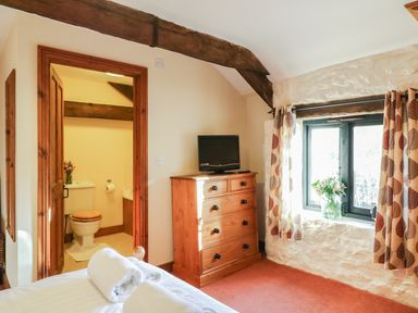 A bedroom with a wooden dresser and television next to a window with patterned curtains at Carthorse Cottage in Teignmouth