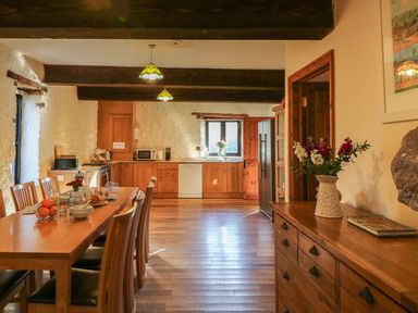 A kitchen and dining area with wooden furniture flowers on a table and sideboard at Carthorse Cottage in Teignmouth