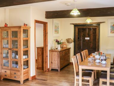 A dining room with a wooden table and chairs a cabinet with glassware a sideboard with flowers and a wooden door at Carthorse Cottage in Teignmouth