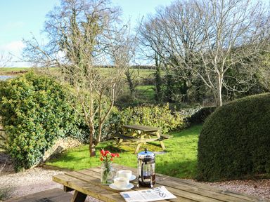 A garden with picnic tables cups flowers and a newspaper on a wooden table at Carthouse Cottage in Teignmouth