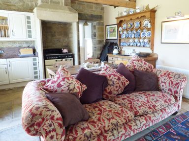 A living room with patterned sofa cushions wooden dining table kitchen cabinets and a plate rack at Humbleton Cottage in Haydon Bridge near Hexham