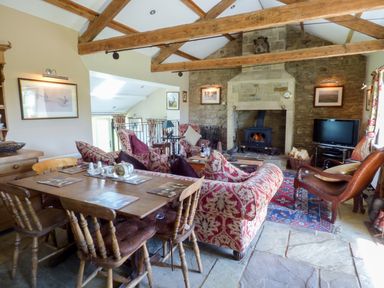 A living room with wooden dining table chairs red patterned sofas a stone fireplace and a television at Humbleton Cottage Haydon Bridge near Hexham