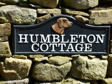 A stone wall with a sign that reads HUMBLETON COTTAGE with a dog head sculpture above the text at Humbleton Cottage in Haydon Bridge near Hexham