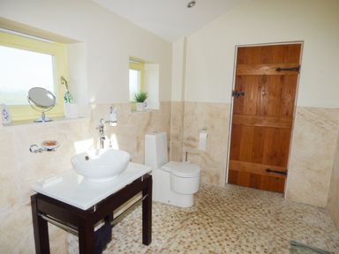 A bathroom with a sink on a wooden stand a toilet two windows and a wooden door at Humbleton Cottage in Haydon Bridge near Hexham